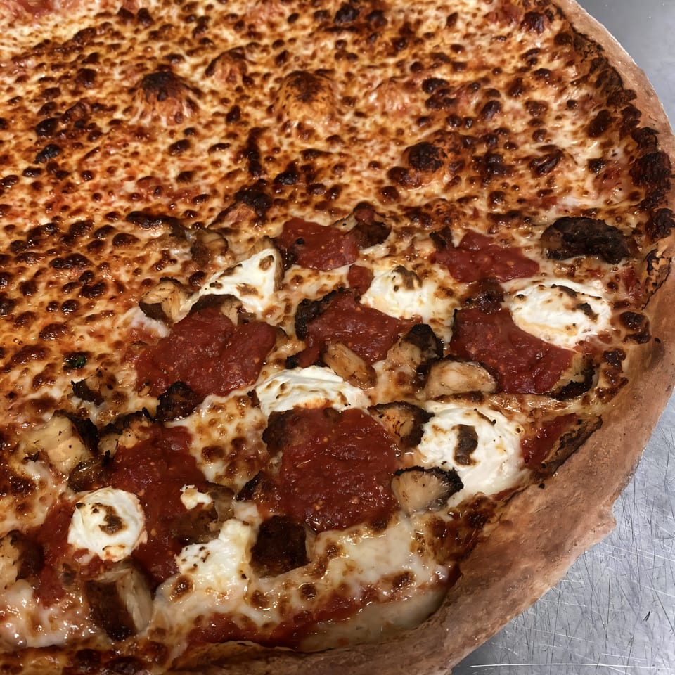 Close-up of a Kabylos Pizza with half plain cheese and half with red sauce, ricotta, and chicken.
