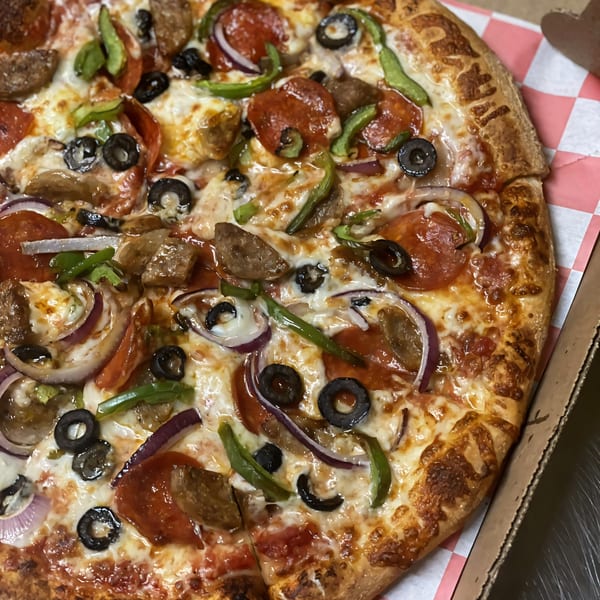 Close-up of a Kabylos Pizza with pepperoni, sausage, green peppers, red onion, and black olives.